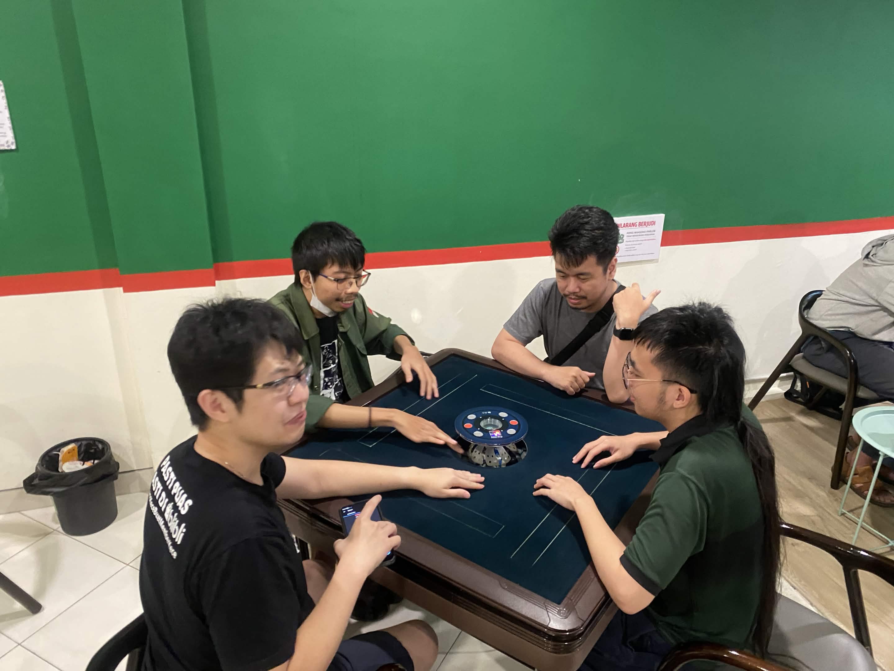 Empat anggota SURIMA duduk mengelilingi meja mahjong otomatis